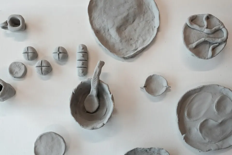 Grey clay plates, bowls, cups and a spoon laid out on a white surface, seen from above.