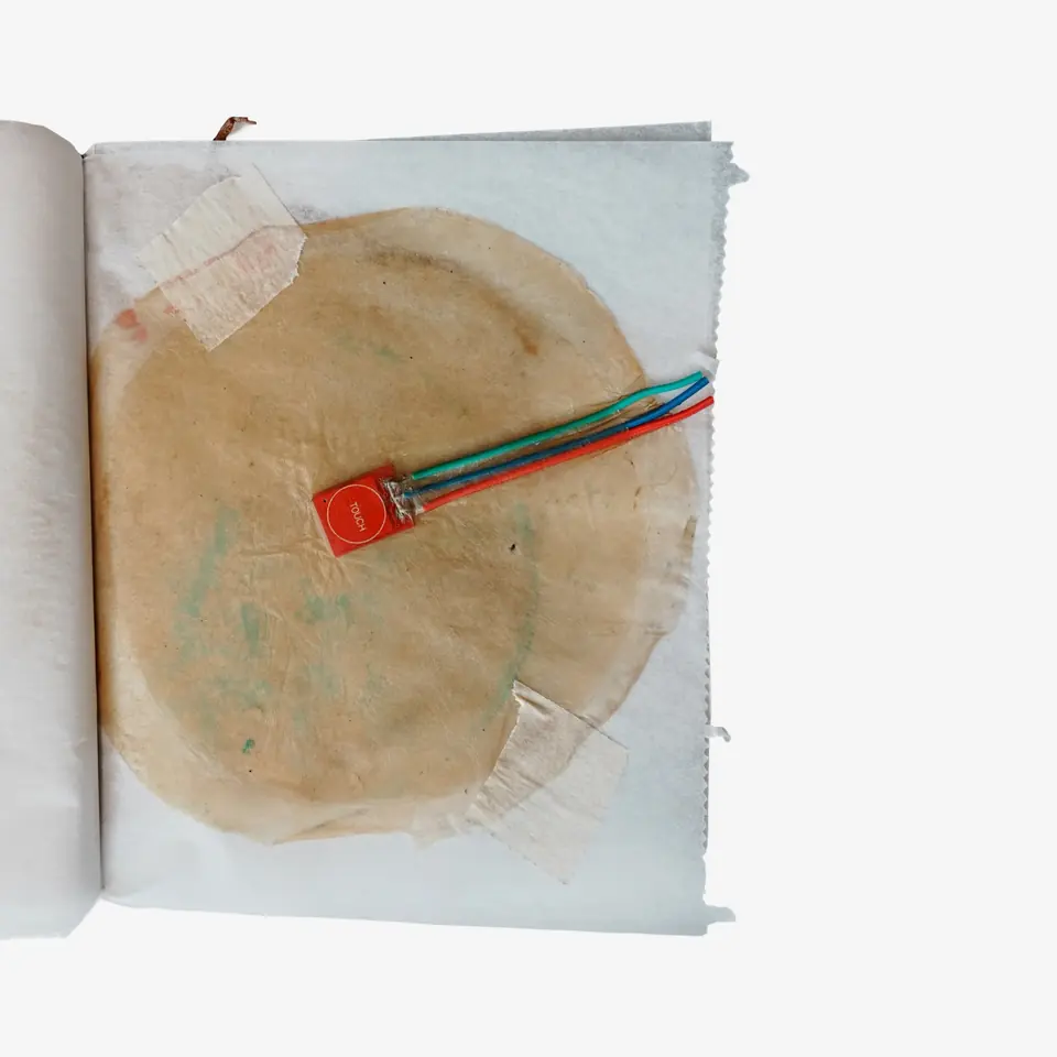 A booklet page with a large tan sheet and a small red board with coloured wires on it.