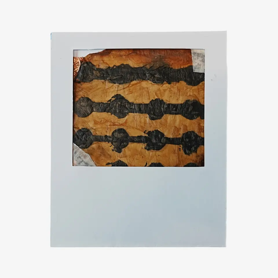 An amber sheet with rows of black painted shapes, mounted in a white card frame.