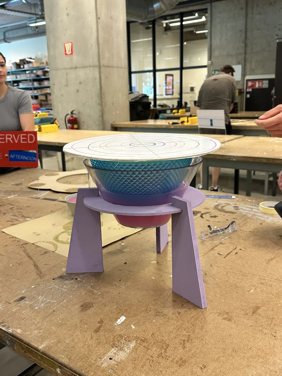 A glass bowl on purple legs in the workshop, with a round top resting on it.