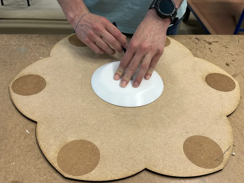 Hands press a white plate onto a flower-shaped wooden board with cork circles.