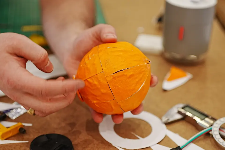 Hands fit a half-finished orange shell over electronics on the workbench.