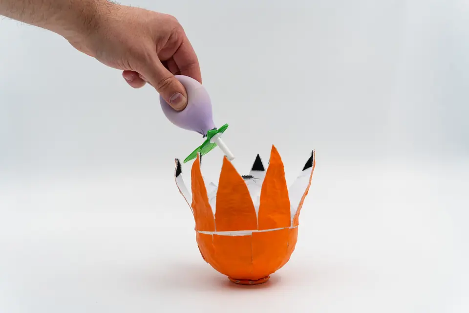 A hand lowers a soft lavender dropper into an orange sphere whose peel segments stand open.