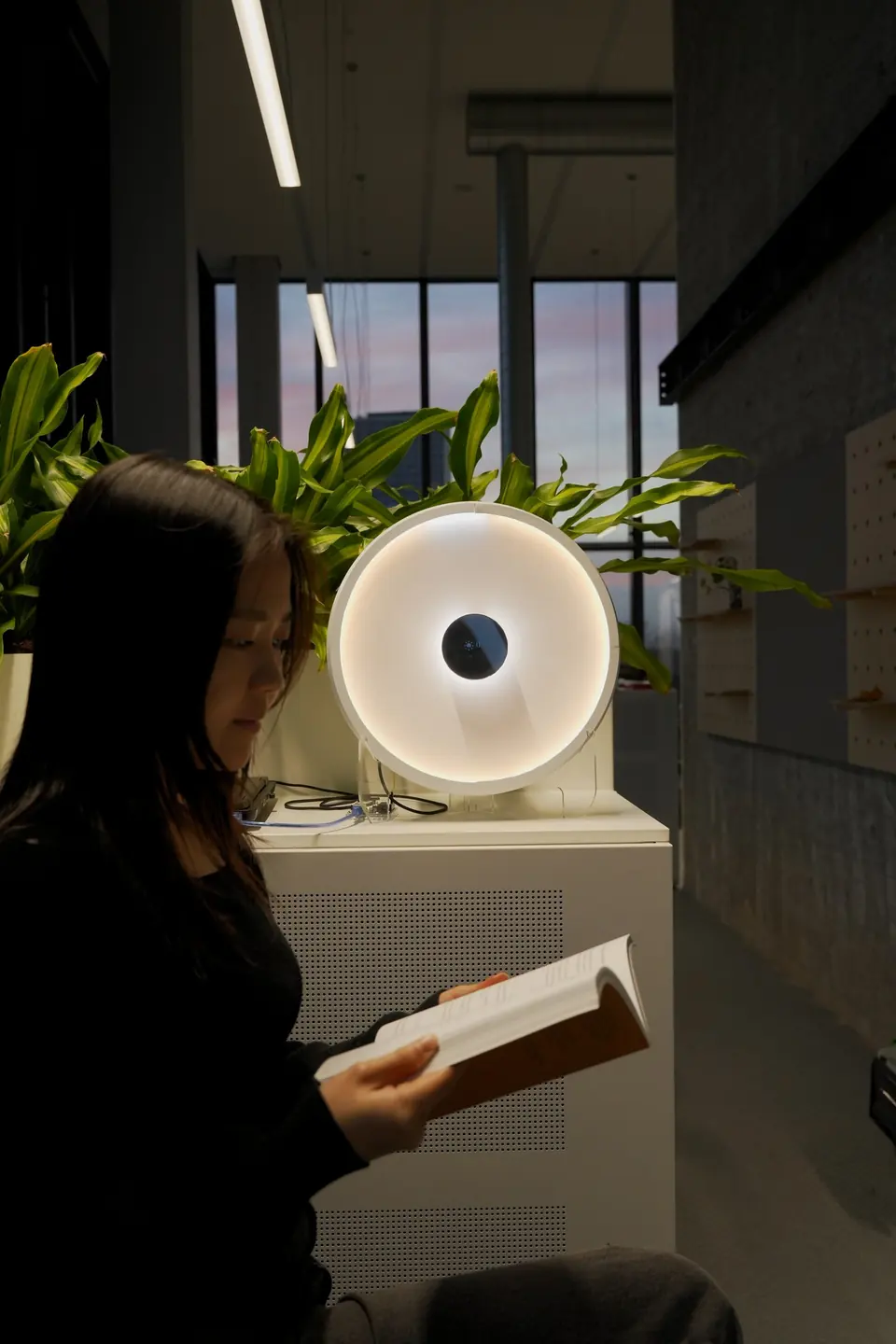 Carecast glows beside a person reading, city lights behind the window.