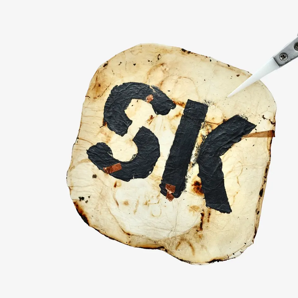 A pale, scorched-looking dried sheet with the letters SK painted in thick black ink.