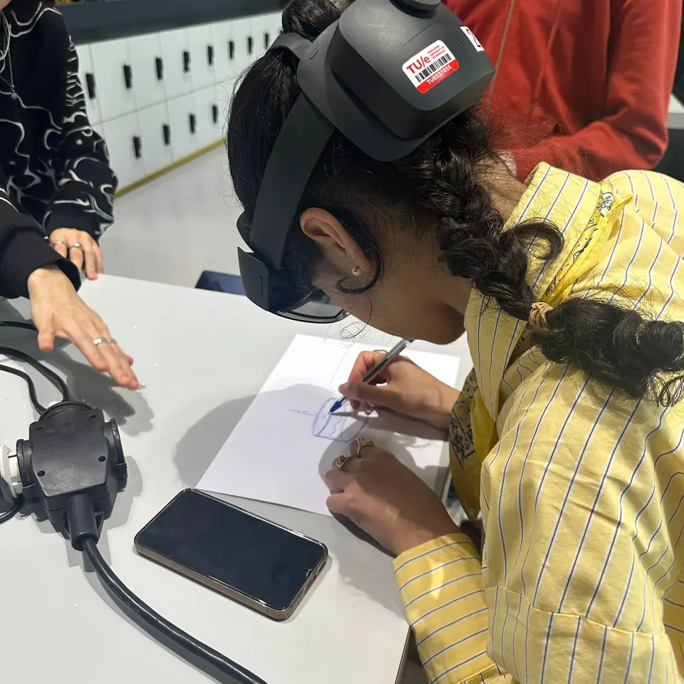 A participant wearing a HoloLens 2 sketches with a pen on paper at a table.
