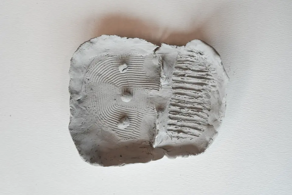 A square clay plate with a combed zone, a ridged zone and three small dots.
