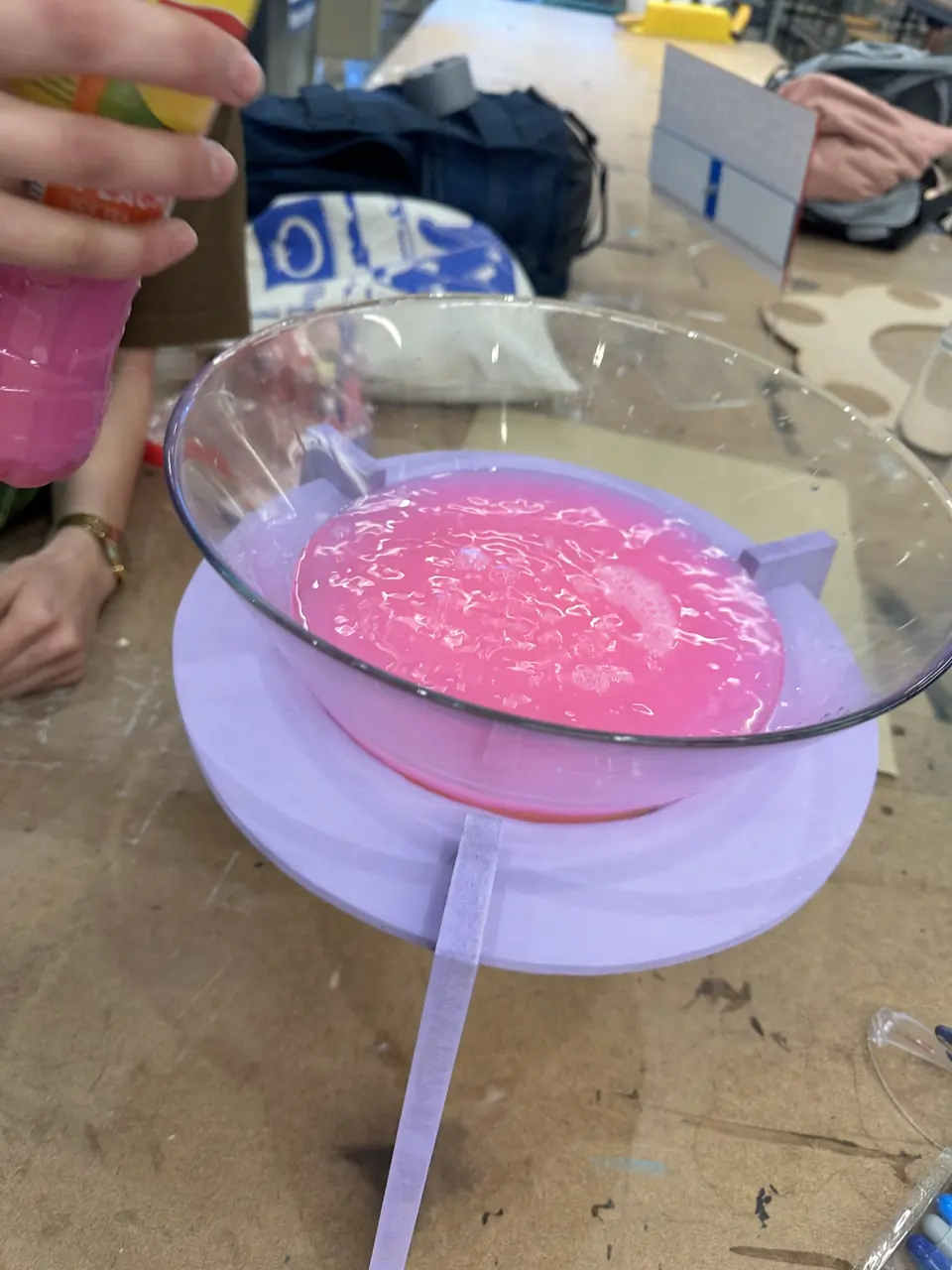 Pink swollen water beads in a clear glass bowl on a purple stand.