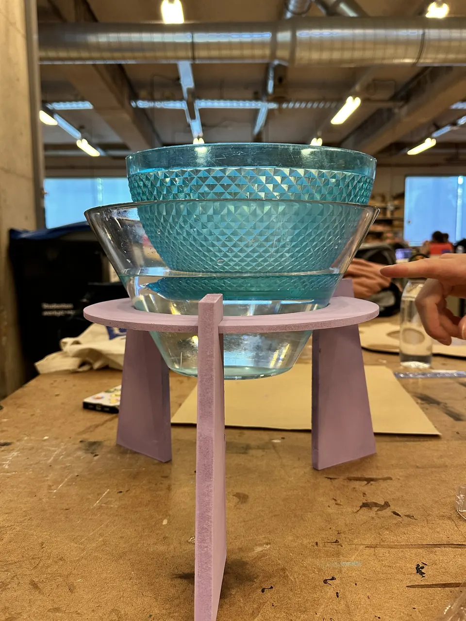 A turquoise glass bowl floating in a clear bowl of water on a pink stand in the workshop.