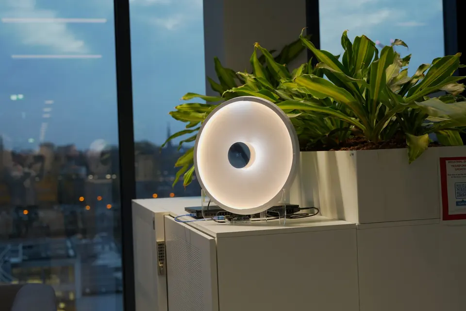 The round Carecast device glowing on a cabinet by a window at dusk.